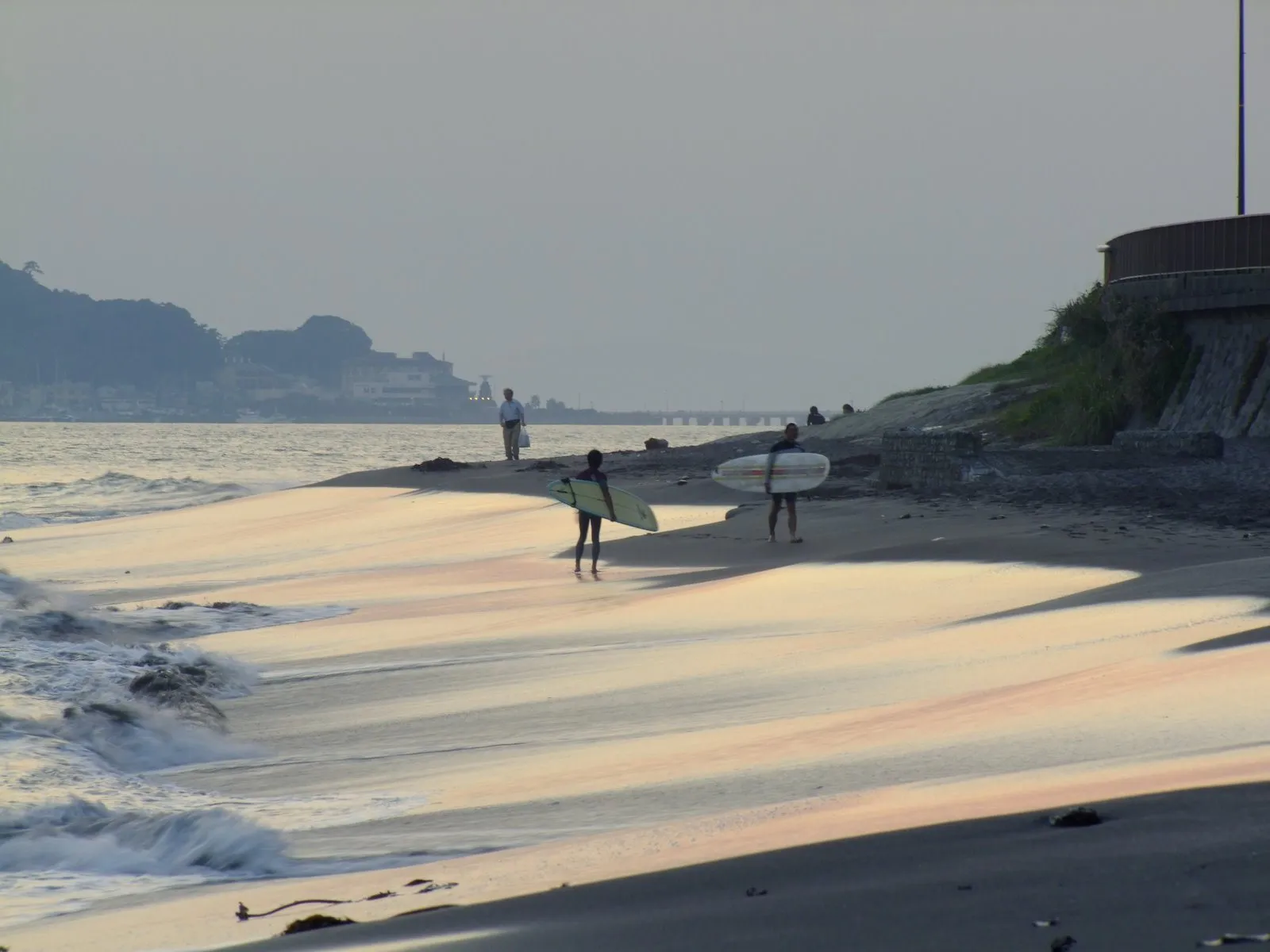 朝の浜辺でサーフボードを手に海へ向かうサーファーたち
